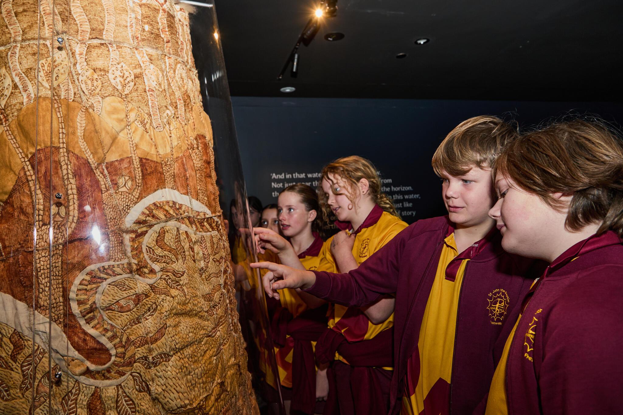 Group of students in a maroon and yellow school uniform looking a possim skin cloak.