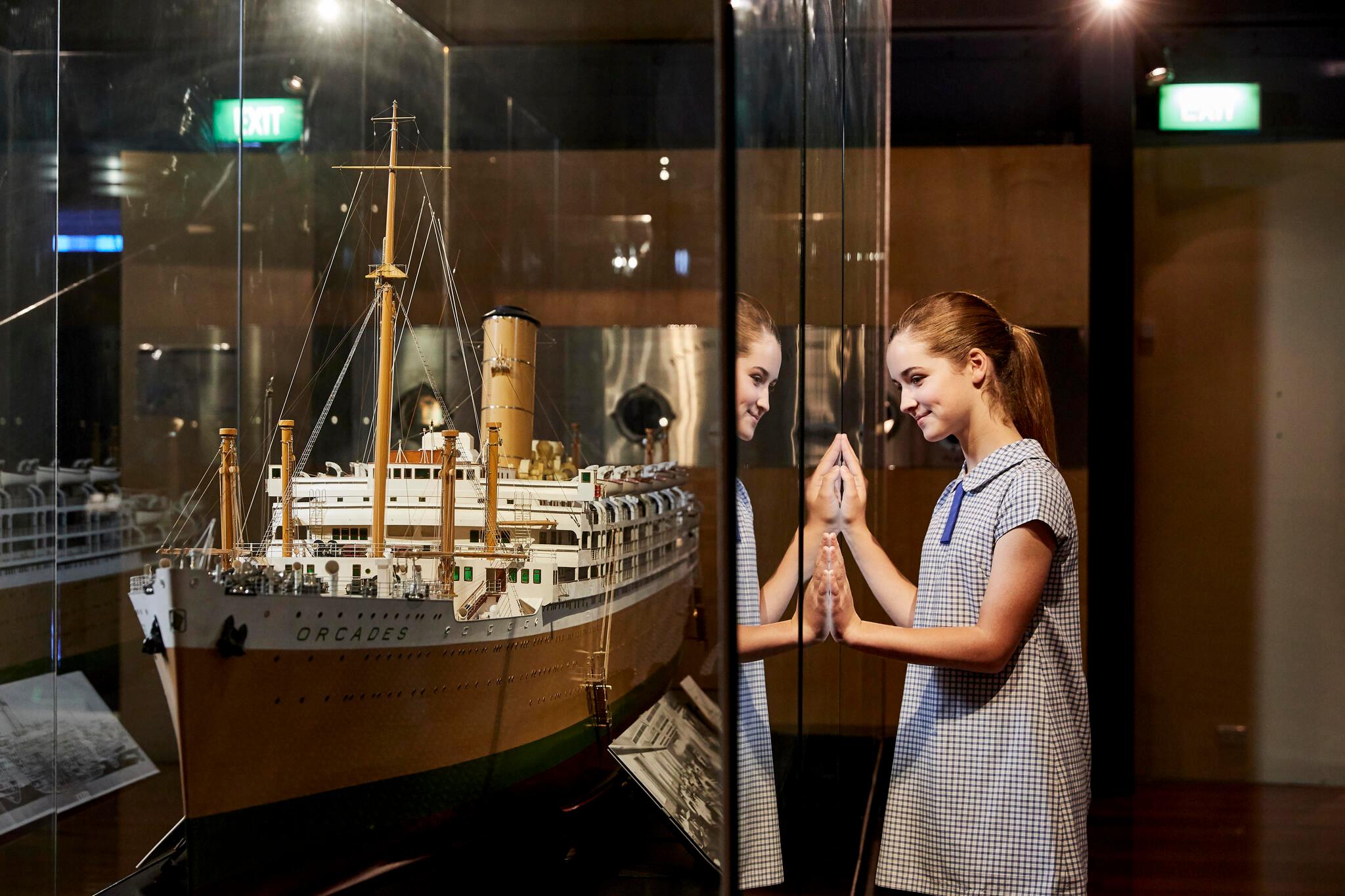 Photo of a girl in a schol uniform looking through a glass case at a large model ship.