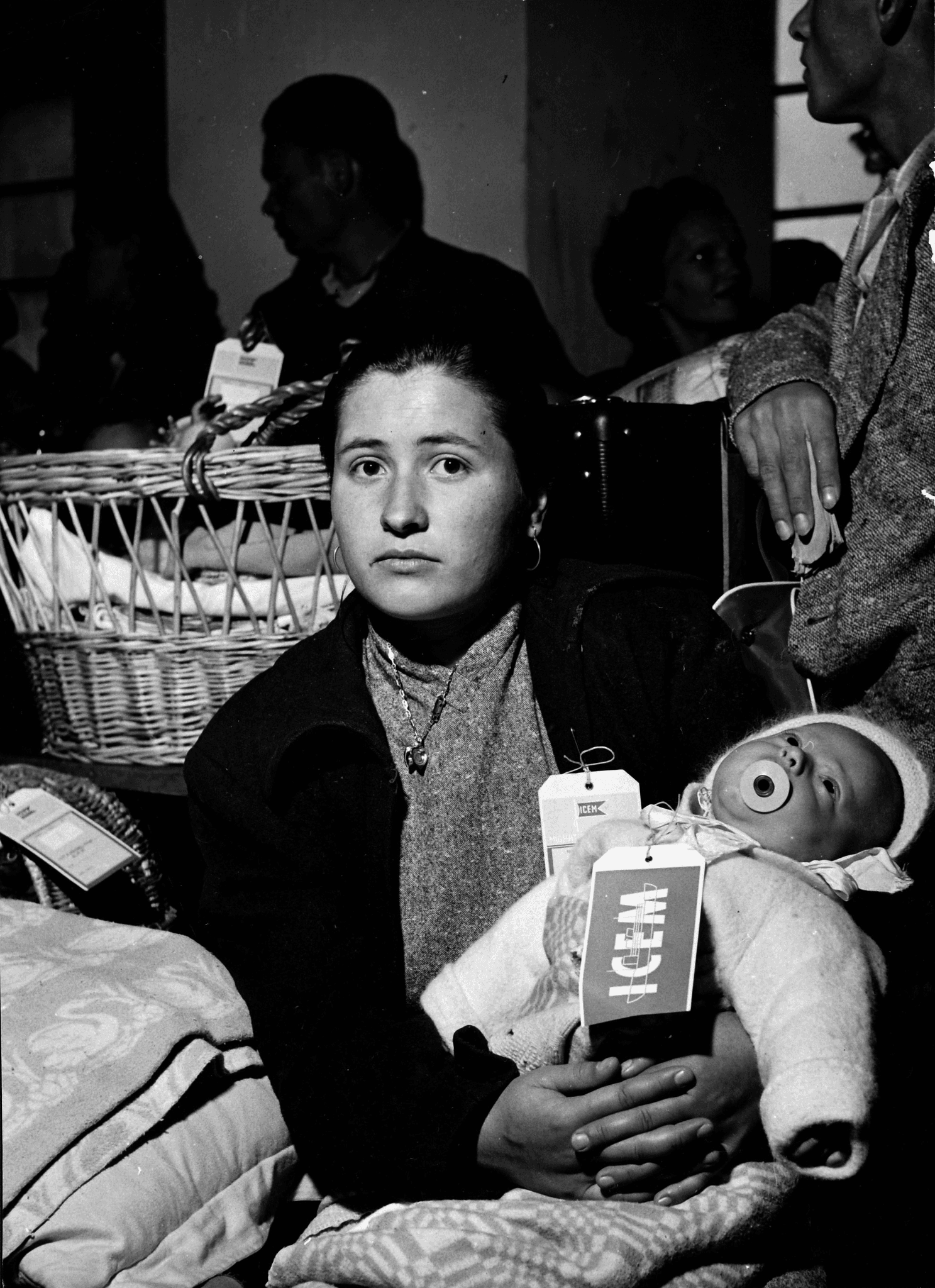 black and white photograph of a young adult female, woollen cardigan and jumper, child in arms. Child has woollen clothes, bonnet, dummy.