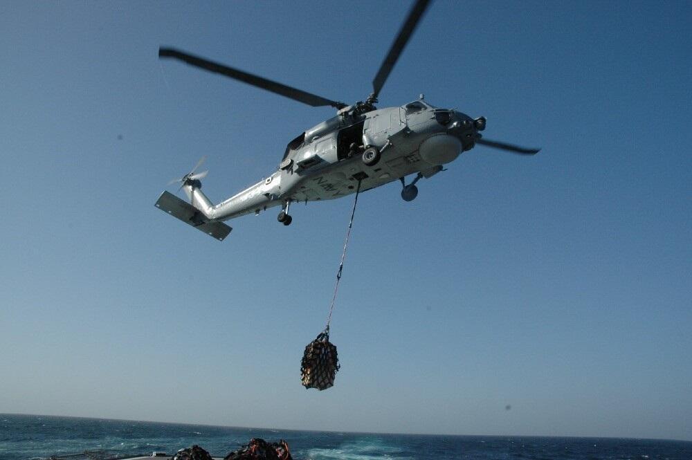 A helicopter flying, a bag of cargo hanging below it. 