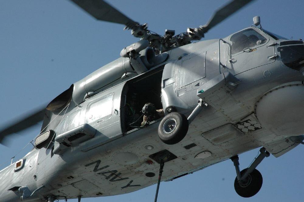 A person looking out the open door of a grey navy helicopter in flight