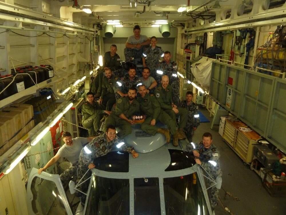 A group of mulirary personel climbiing on top of a grey mulitary helicopter.