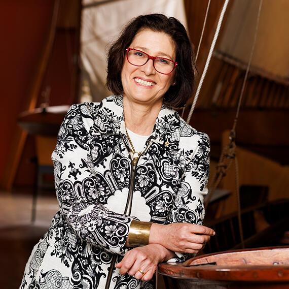 Portrait photograph of a woman with dark hair and red glasses, wearing a black and white floral patterned jacket.