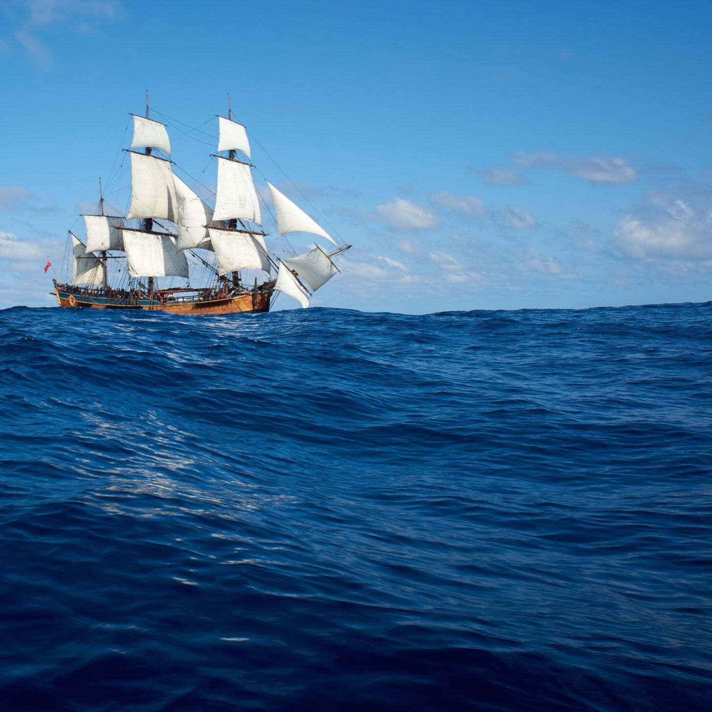 wooden tall ship with white sails on the ocean with a blue sky 