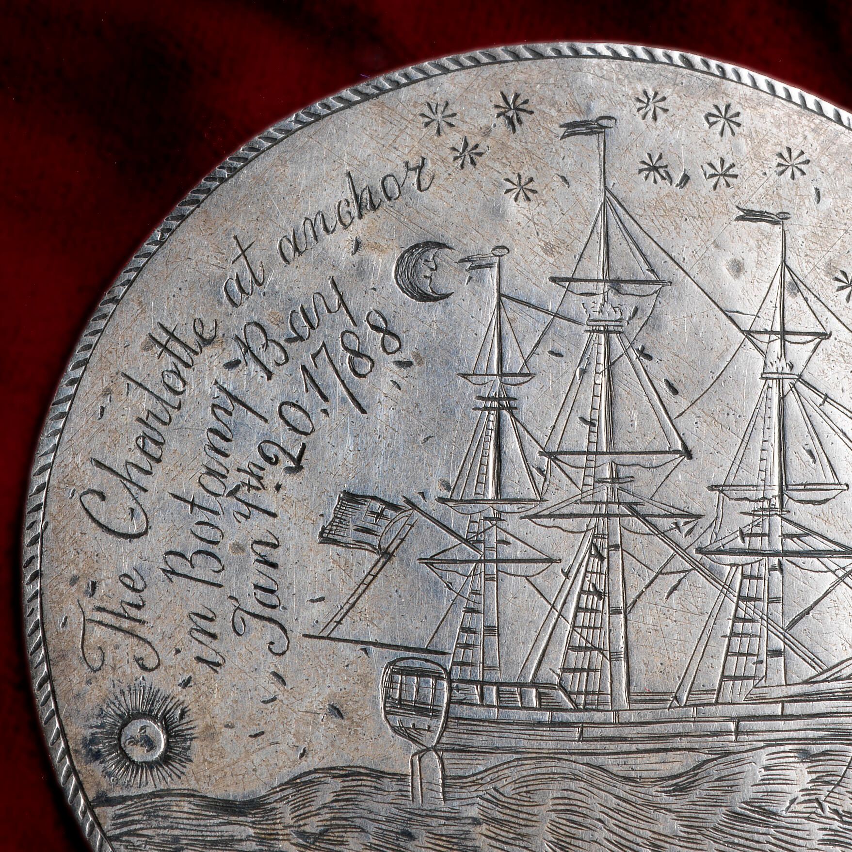 The CHARLOTTE Medal, a silver disc engraved on both sides. This photograph shows engraved a fully-rigged ship, the sun is near the horizon line on the lower left whilst a crescent moon and stars are inscribed on the upper right. Above are inscribed the words 'The CHARLOTTE at anchor / in Botany Bay / Jany. th 20, / 1788'.