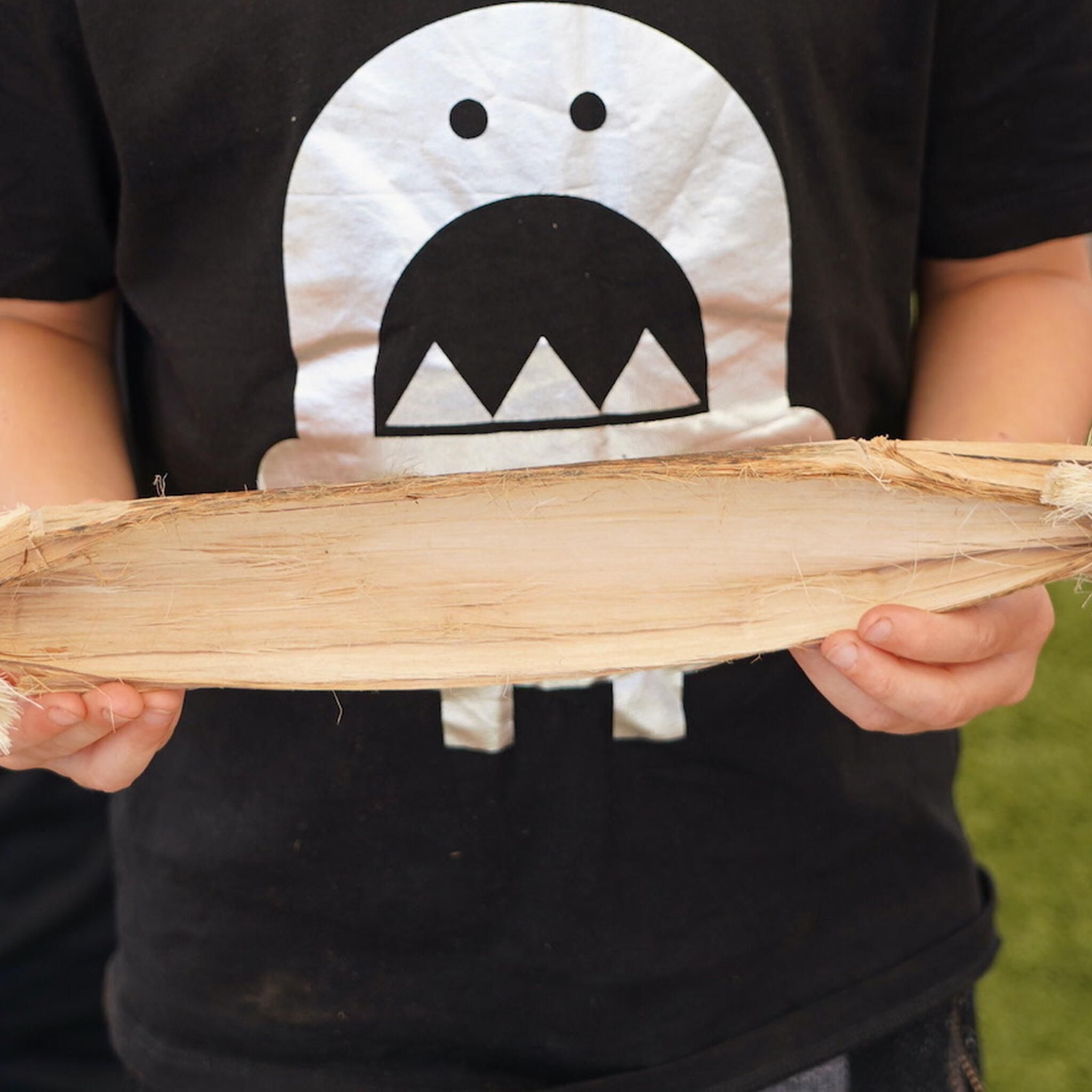 The torso of a boy with a black t-shirt holding a small model of a bark canoe, around 40cm long. 