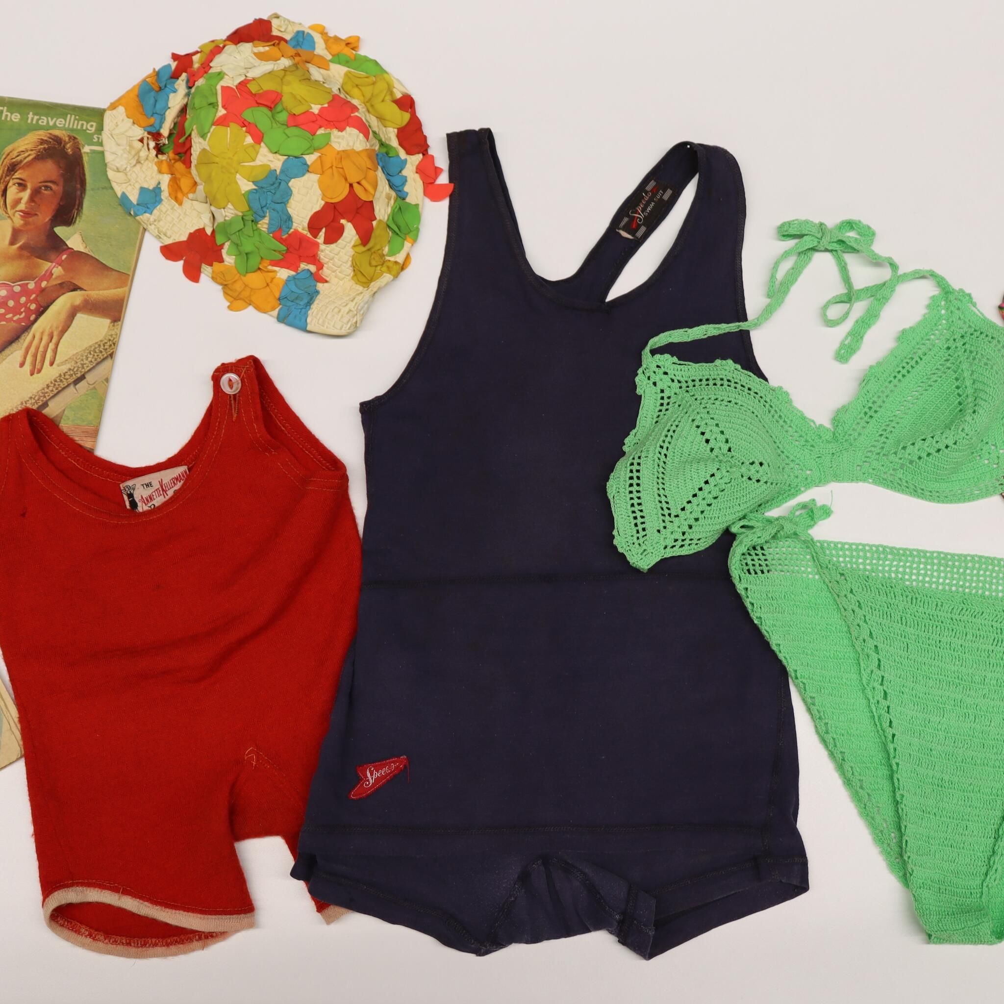 collection of swimwear in different colours and styles from different time periods, as well as 2 old magazines and a floral swimming cap. 