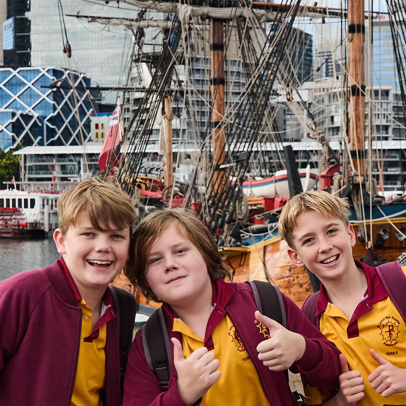 Photo of a group of 3 boys in schol uniforms, with the tall ship Endeavour behind them.