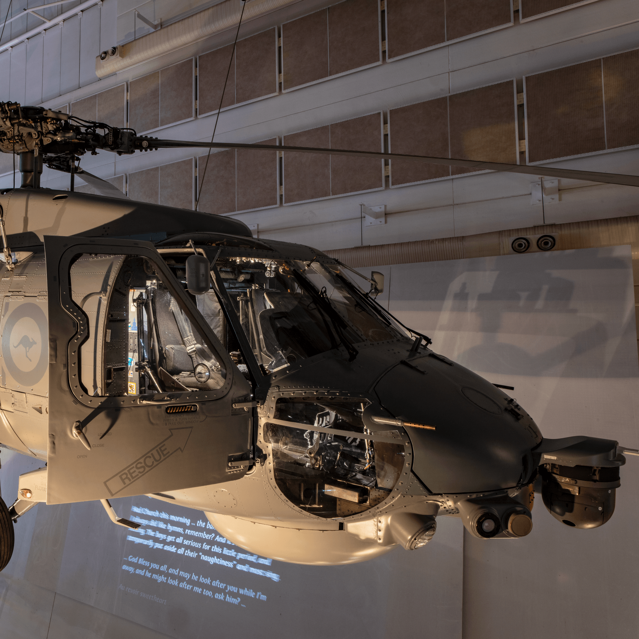 Milirary helicopter, mostly grey with orange and black tiger stripes painted on its tail, hung inside a museum gallery.  