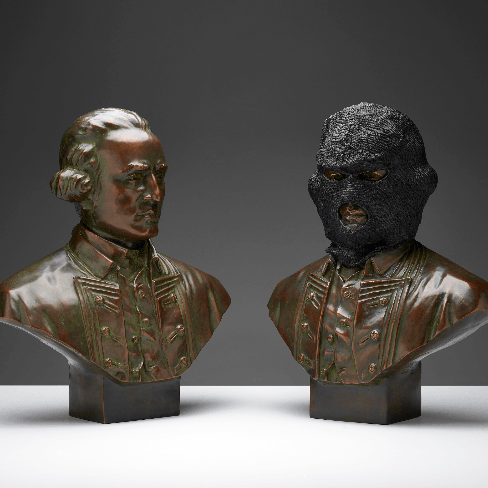 2 bronze sculptures of a bust of a man, the right one with a black  