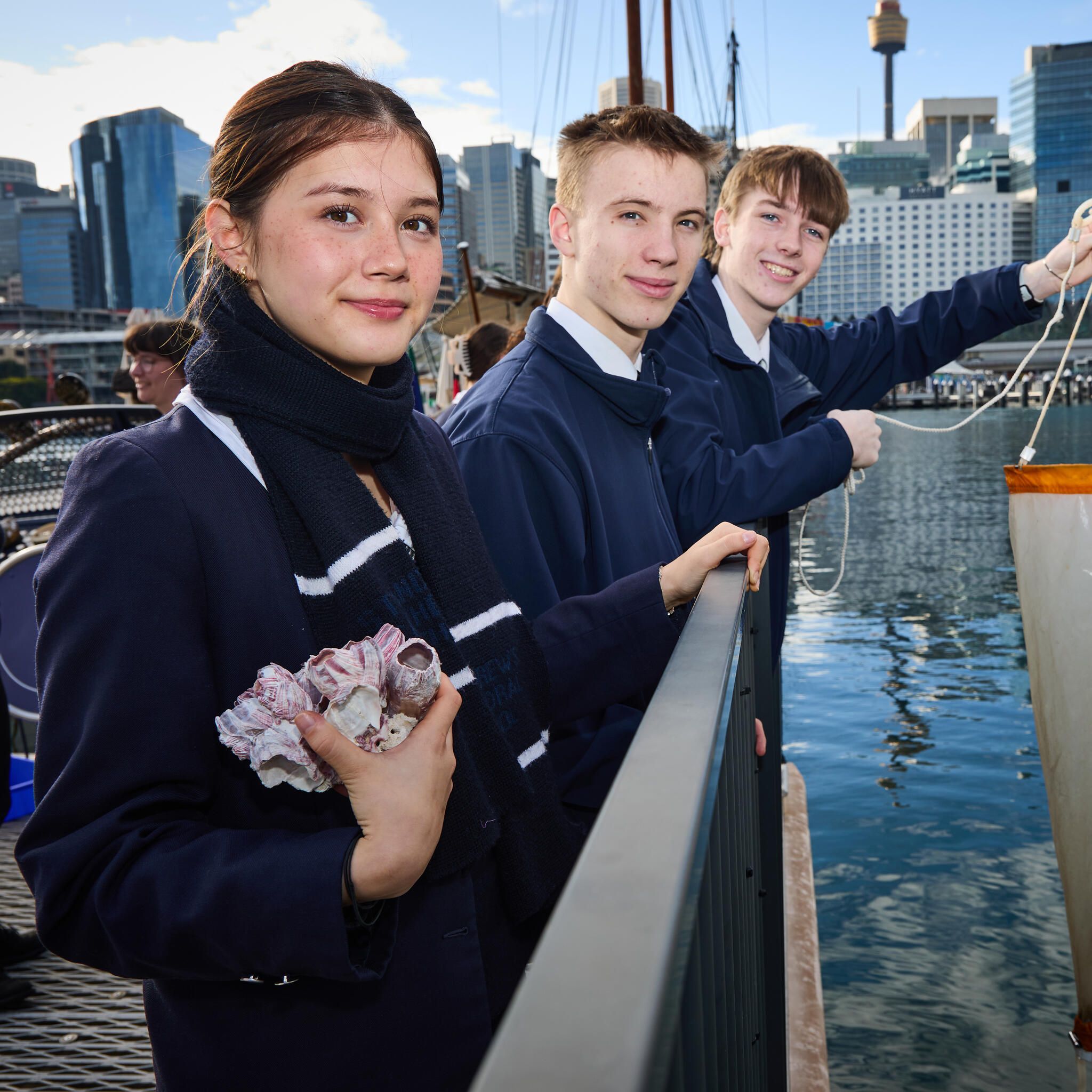 3 high school students in navy uniform on the museum wharf with sydney in the background.