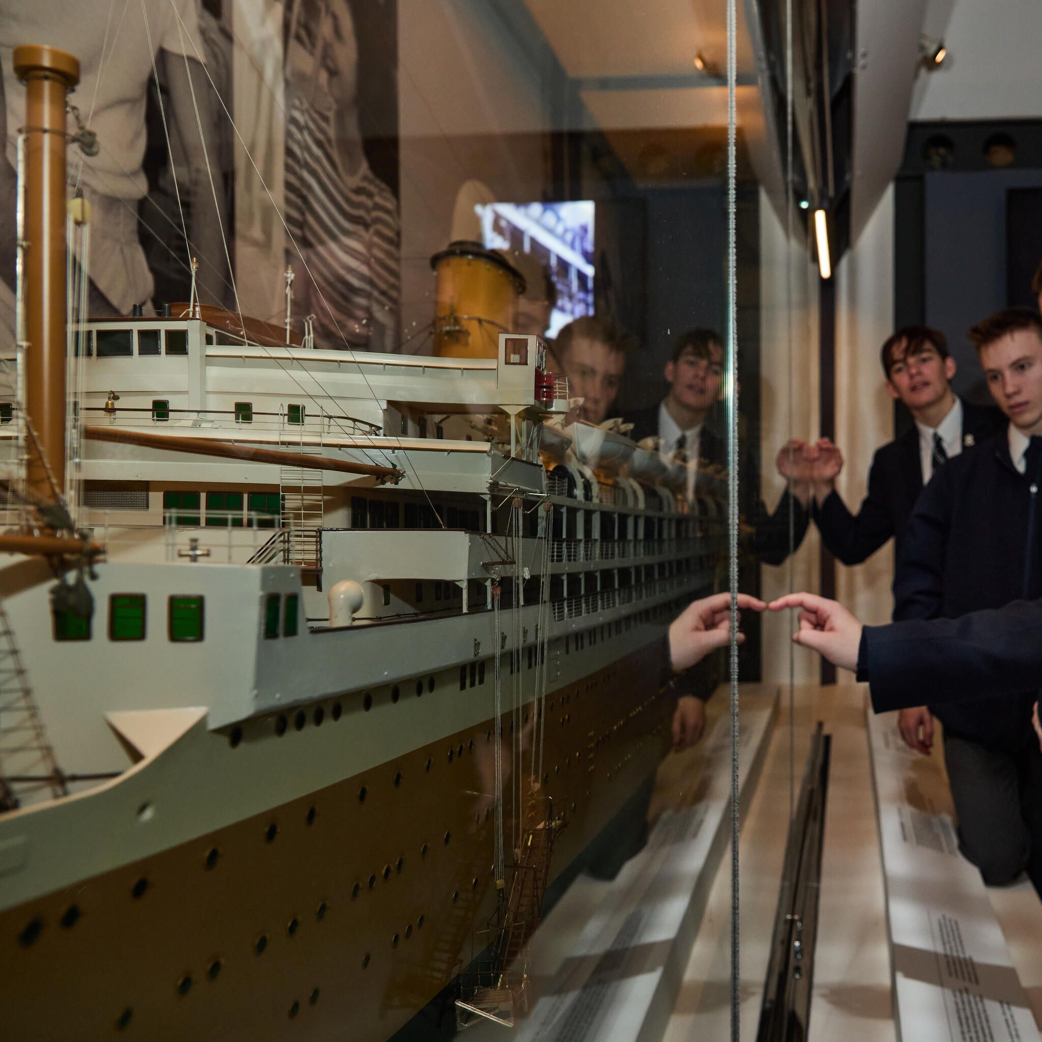 image of a model of an ocean liner in a display case, with a line of high school students looking at it. 