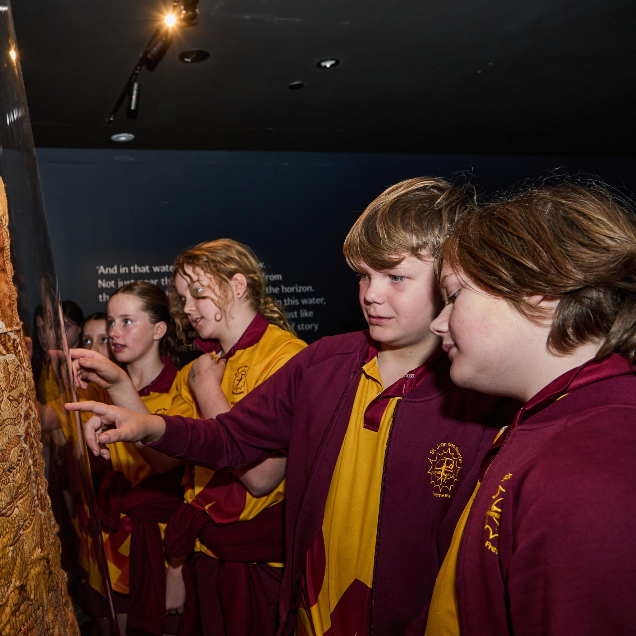 Group of students in a maroon and yellow school uniform looking a possim skin cloak.