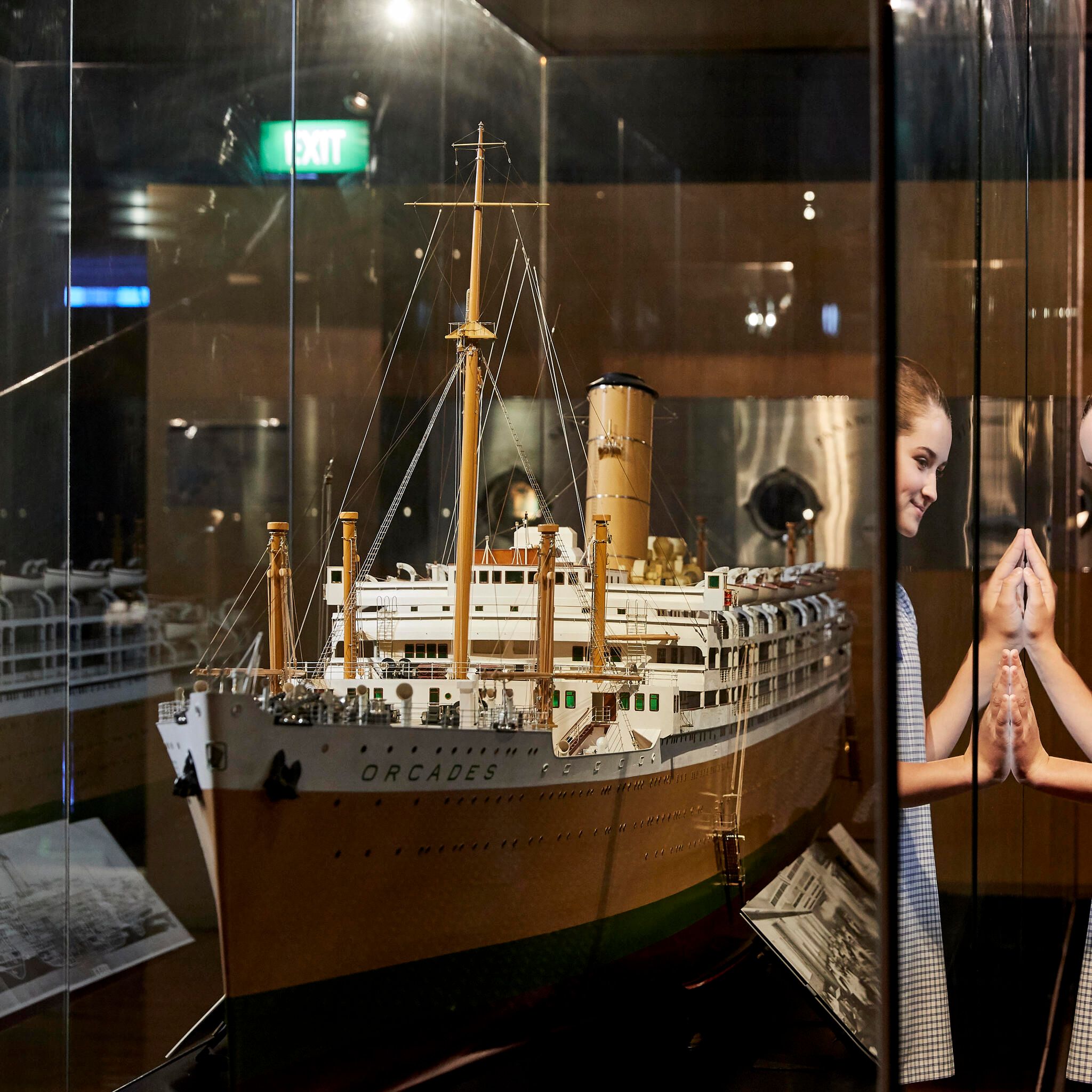 Photo of a girl in a schol uniform looking through a glass case at a large model ship.