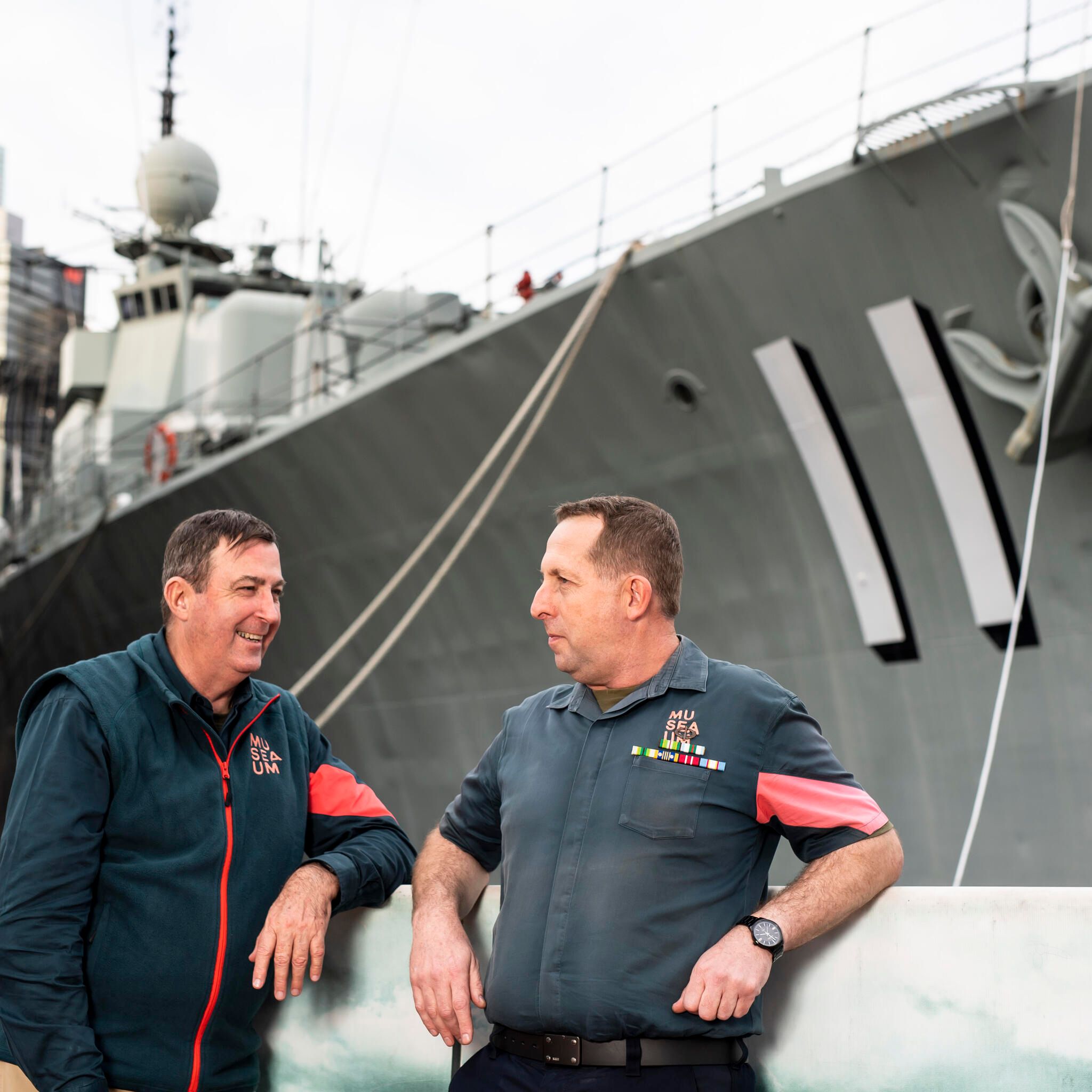 2 men in volunteer uniforms with the navy destroyer VAMPIRE in the background