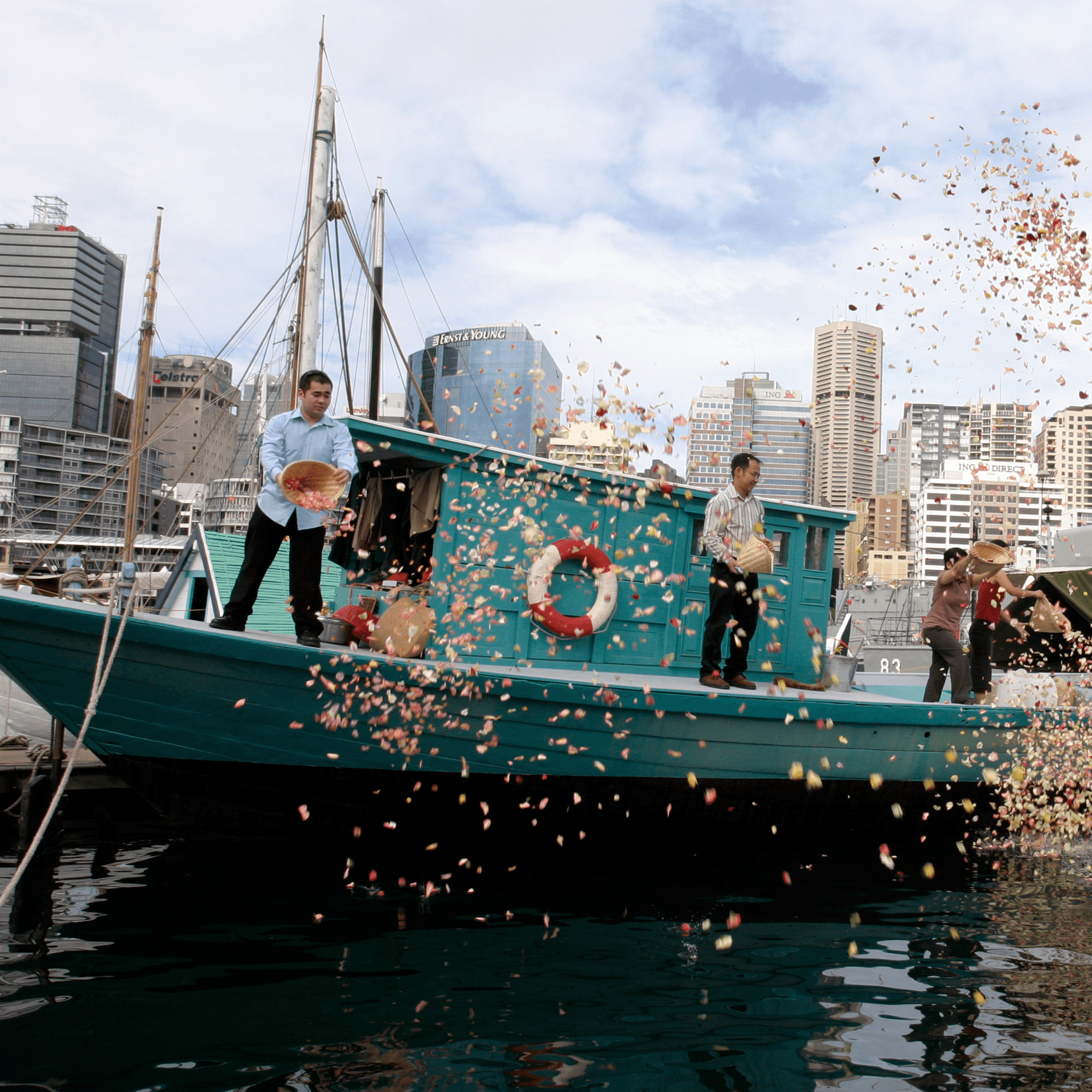 Blue Fishing Boat. Standing on board are the Lu family members who came to Australia from Vietnam as refugees on board the boat. They are scattering flower petals into the harbour in celebration.