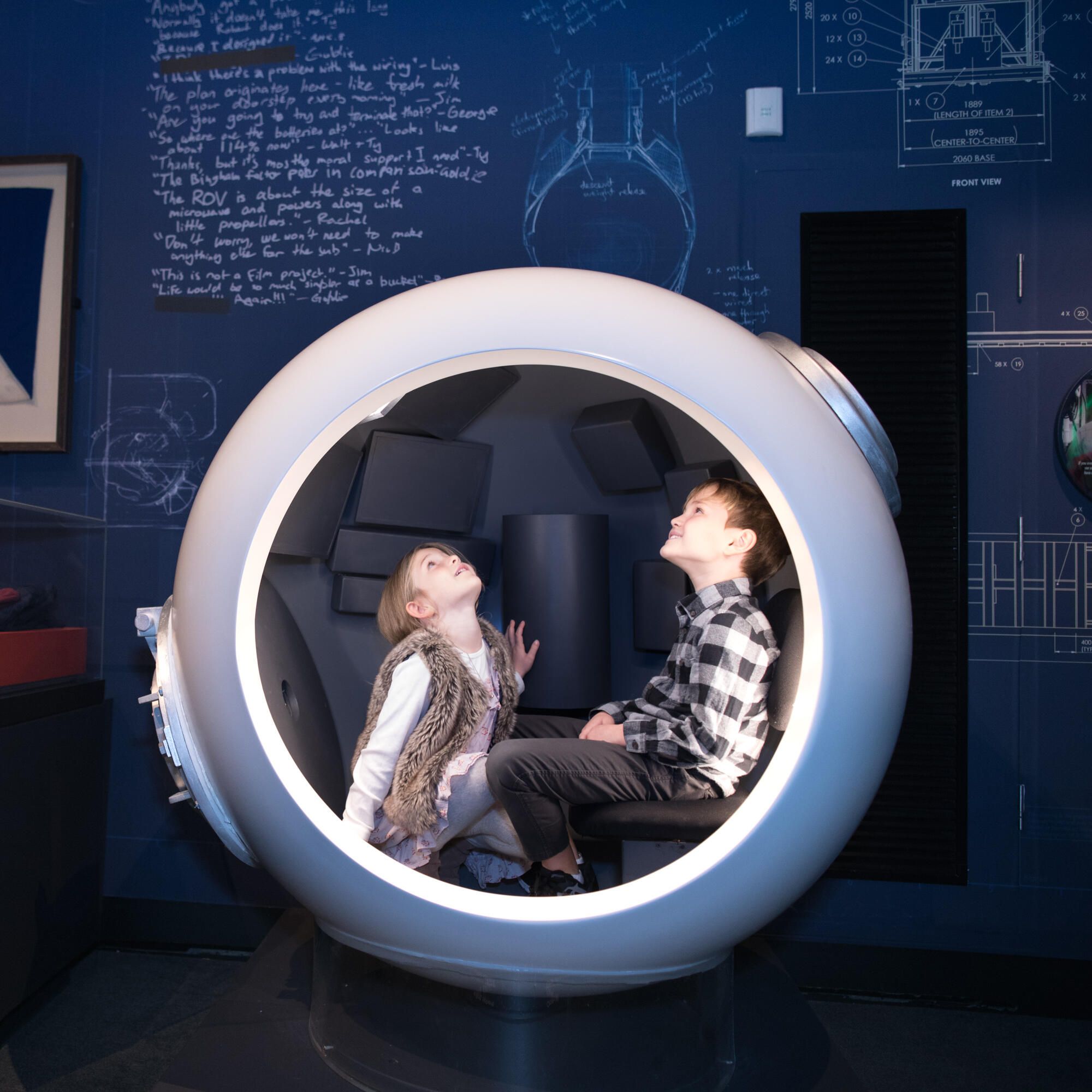 Photo taken inside an exhibition of two children in a round sphere looking up. 