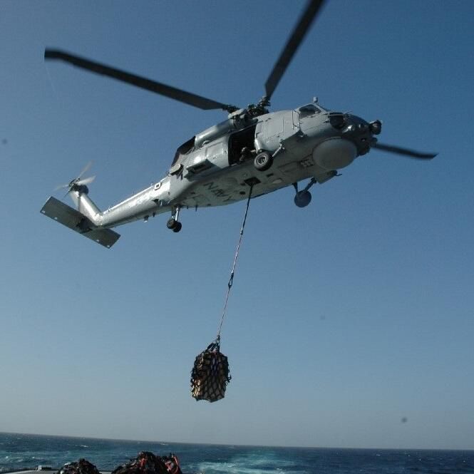 A helicopter flying, a bag of cargo hanging below it. 