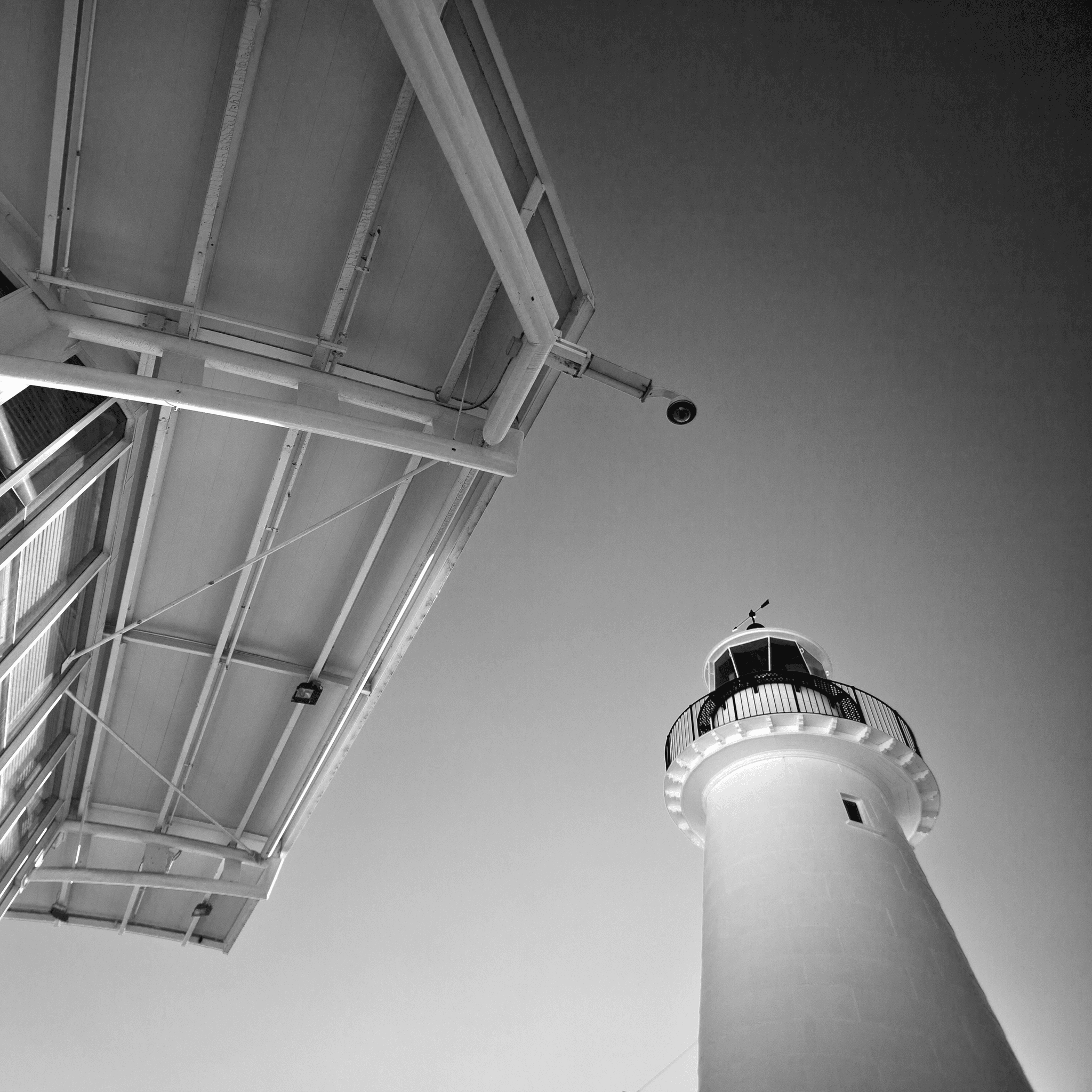 Black and white drematic photo looking up at the edge of a modern building and a lighthouse. 